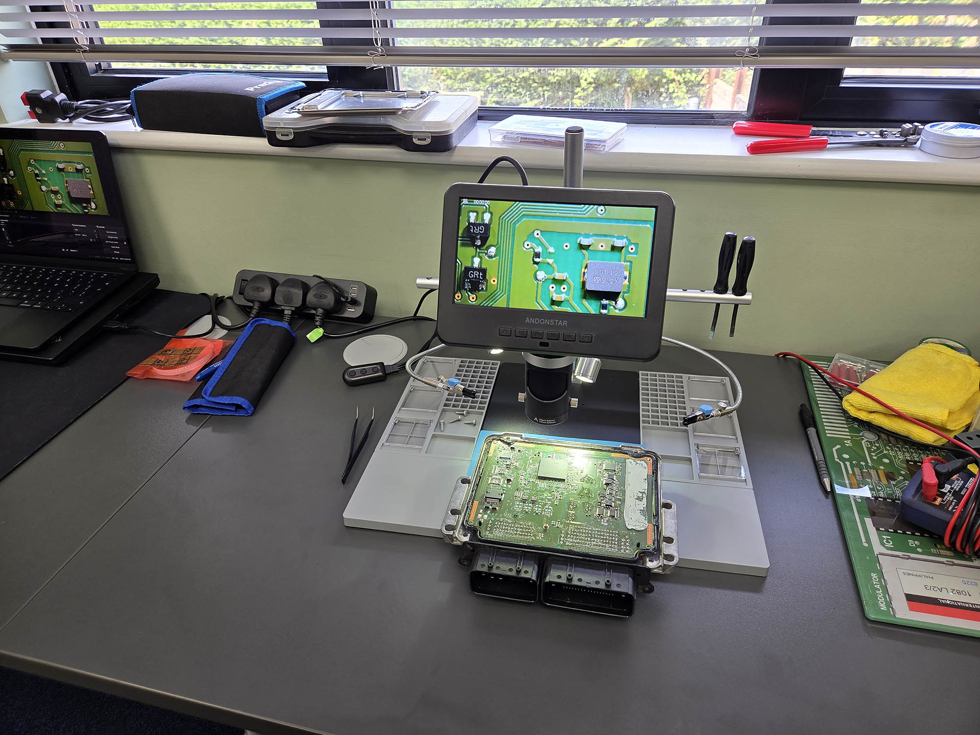 Bosch ECU circuit board on the ByteFLASH bench under a digital microscope, with the board detail shown on the microscope screen